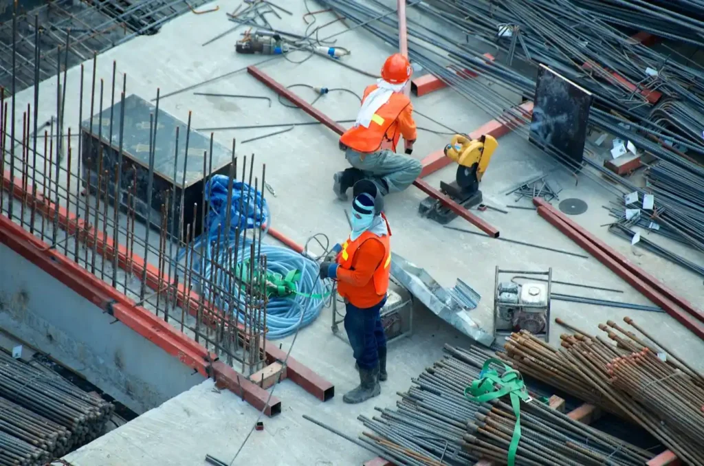 Construction workers in safety high-visibility gear working with steel rebar and equipment on a building site.