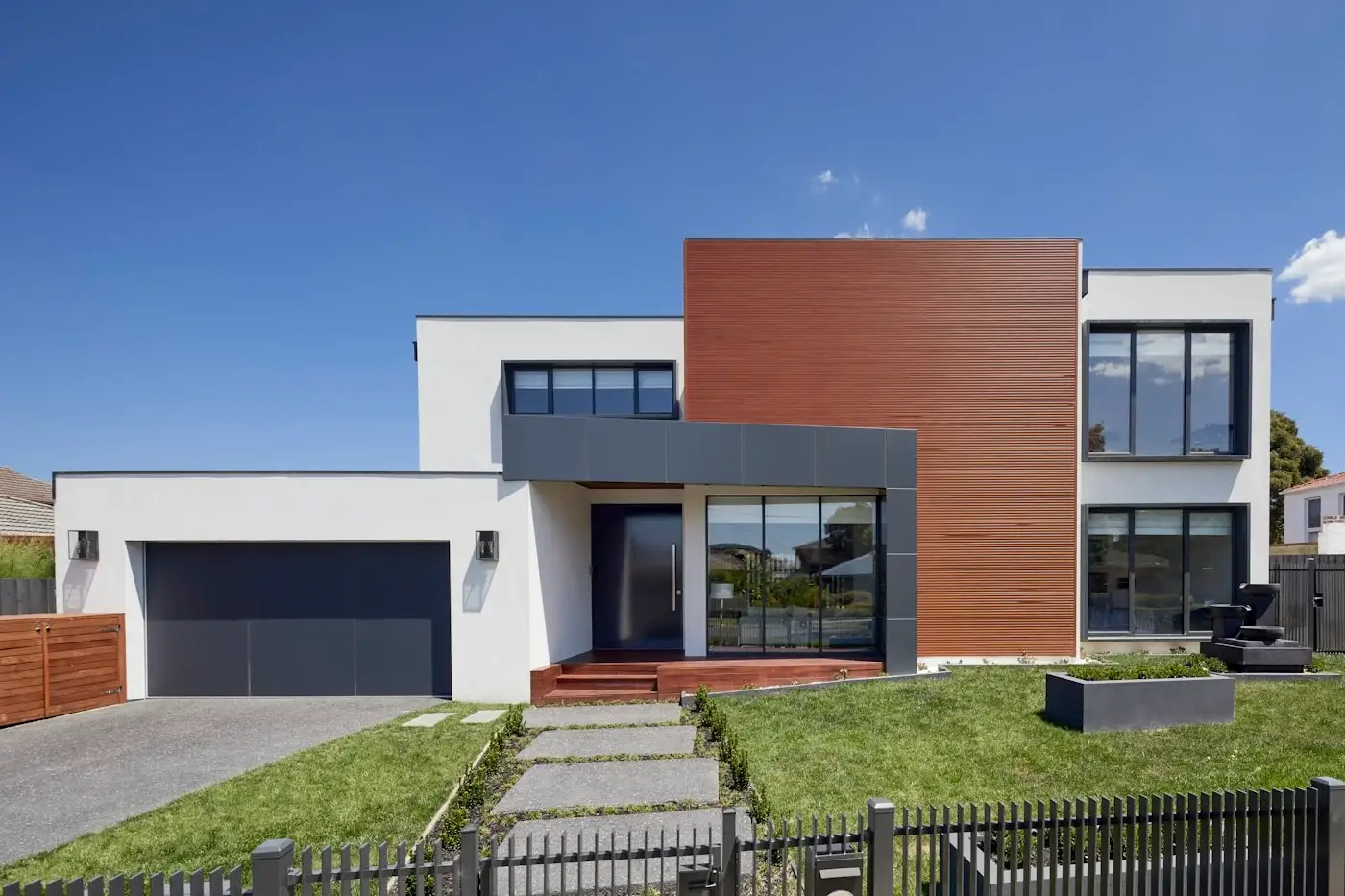 Modern two-story residential home exterior featuring white stucco, wood panel siding, dark trim, and landscaped lawn after full renovation.