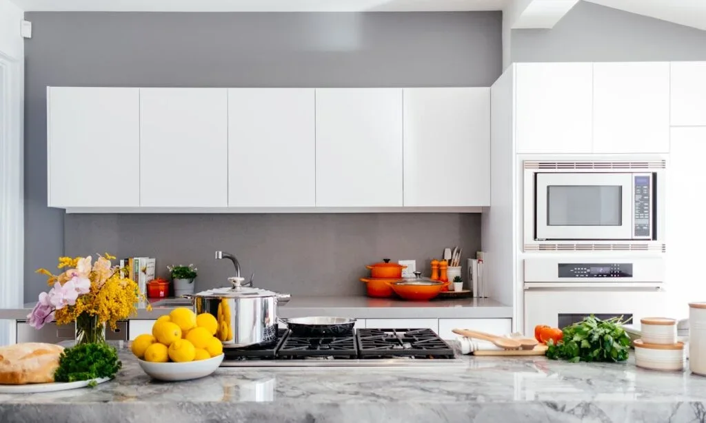 Modern kitchen renovation featuring white flat-panel cabinets, grey backsplash, marble countertop, and built-in wall ovens.