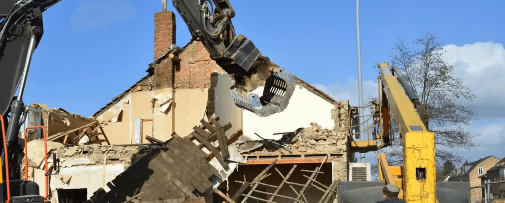 Excavator claw attachment tearing down a brick house frame during residential demolition
